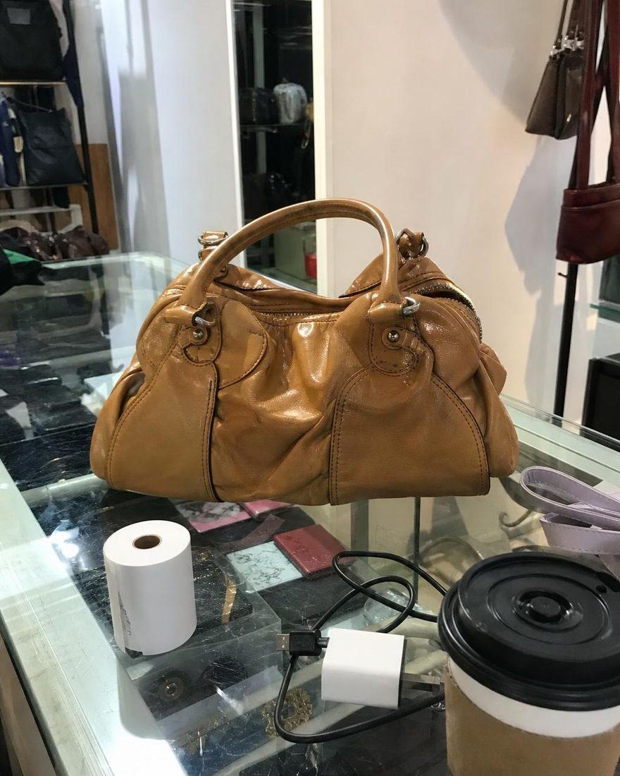 Handyfoto einer Ledertasche auf der Theke zwischen Kassenrolle und Kaffeebecher