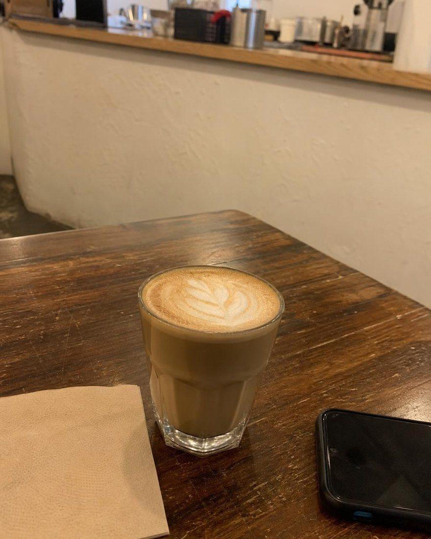 Handyfoto eines Milchkaffees auf einem Holztisch neben einem Handy