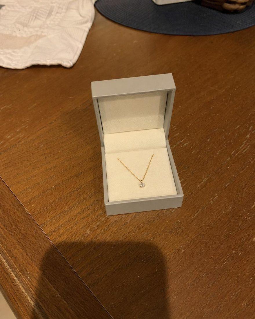 Handyfoto einer Kette mit Diamantanhänger in einer offenen Schachtel auf einem Holztisch