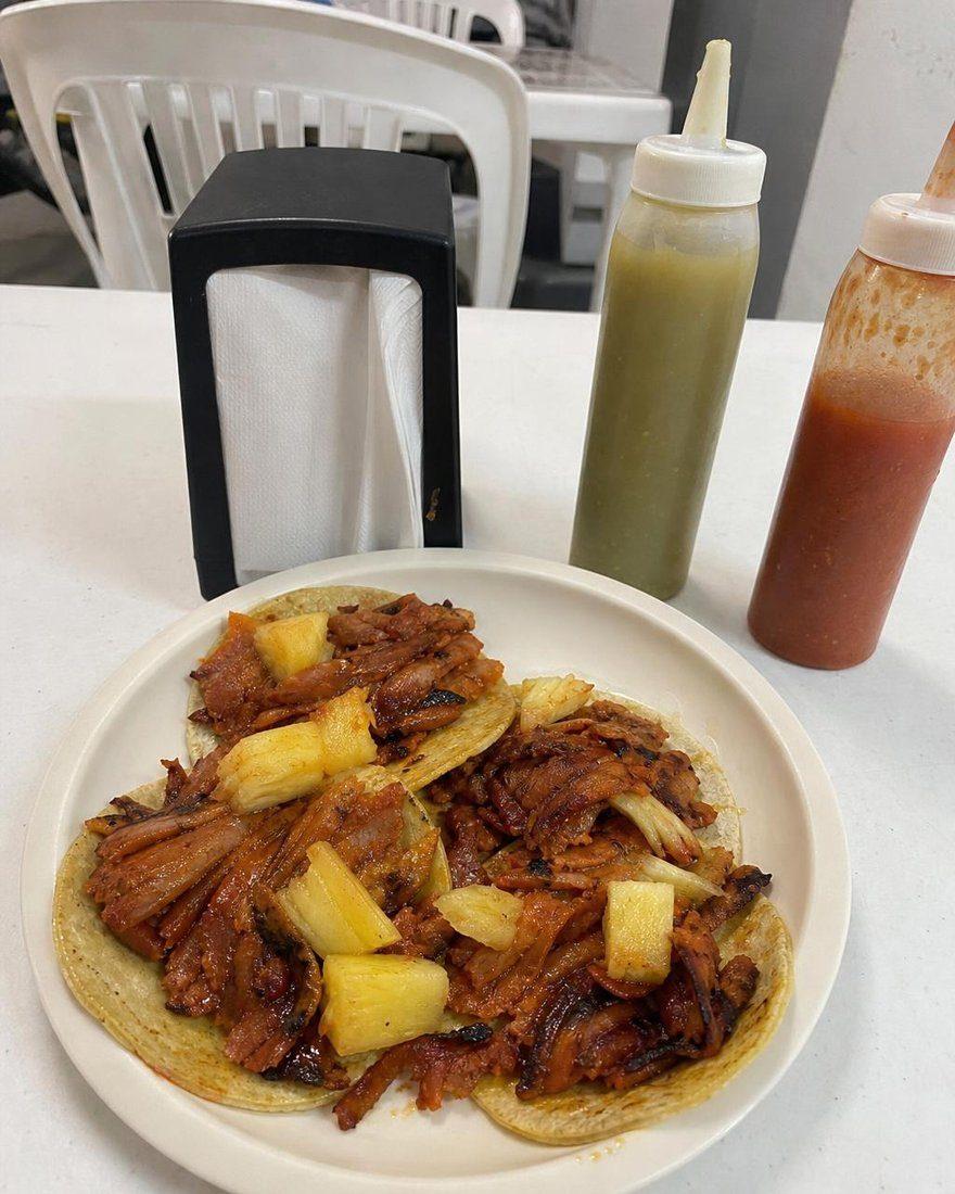Handyfoto eines Tellers Tacos al Pastor mit Ananas auf einem Tisch mit Salsas
